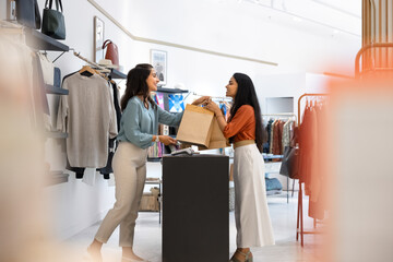 Happy Latin retail store assistant giving shopping bags customer