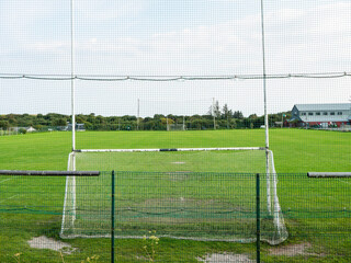 Tall goal post for Irish sport on a small training ground with green field of a small club. Camogie, hurling and rugby training ground.