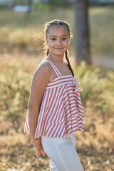Young girl posing in striped summer top in a sunlit outdoor setting during golden hour