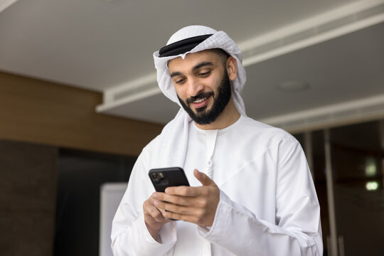 Smiling young middle eastern businessman hold smartphone read message text