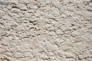 Old white stone wall background. Irregular pattern of antique architectural feature. Sturdy whitewashed house facade in old town, central Spain, Castile-La Mancha. Ancestors culture and craftsmanship.