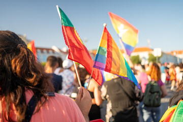 Vibrant crowd of homosexual men and women waving rainbow flags at gay pride parade, celebrating LGBTQ rights in city against bright blue sky