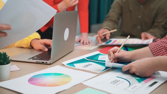 A diverse team working together at a creative workspace, utilizing a laptop and colorful charts to develop business graphics and engage in productive discussions. SACTR