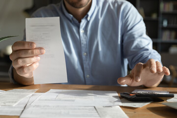 Closeup businessman holding invoice counting on calculator at office desk