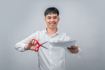 A handsome Asian businessman expresses satisfaction while cutting a financial document with red scissors. This concept is suitable for business, finance, advertising, and debt-free concepts.

