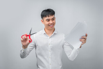 A handsome Asian businessman expresses satisfaction while cutting a financial document with red scissors. This concept is suitable for business, finance, advertising, and debt-free concepts.

