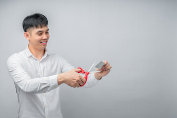 A handsome Asian businessman expresses satisfaction while cutting credit card with red scissors. This concept is suitable for themes of financial freedom, debt reduction, business, and advertising.

