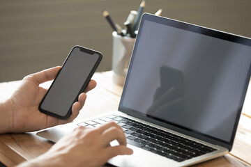 Closeup young man entrepreneur using notebook smartphone at workplace desk