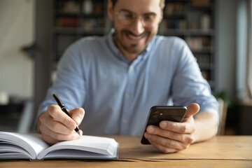 Closeup young businessman holding smartphone writing with pen at desk