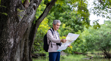 Asian senior man is trekking in the forest while looking at the map for weekend vacation adventure and leisure outdoor activity