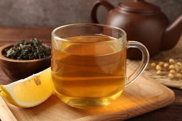 Aromatic tea in cup with lemon, teapot and dry leaves on wooden table, closeup