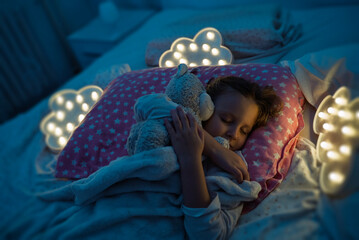 Adorable cute little girl sleeping tight hugging her teddy bear , clouds lights around her 