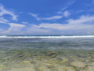 Clear turquoise water over a rocky shoreline under a bright blue sky with soft clouds