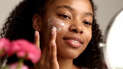 Young african american woman applying face cream to her cheek, smiling and looking in the mirror vector illustration - Powered by Adobe