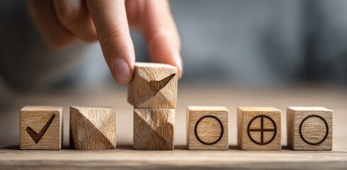 A hand stacks wooden blocks with various symbols, including check marks and circles, on a table