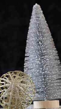 Una toma de cerca de una bola de navidad dorada y un &aacute;rbol plateado rodeados de luces blancas con un fondo desenfocado. Decoraci&oacute;n de navidad y fin de a&ntilde;o. Video Vertical
