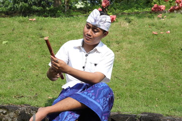 Portrait of Asian man wearing balinese traditional cloth playing bamboo flute in outdoor park