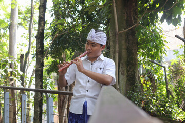 Portrait of Asian man wearing balinese traditional cloth playing bamboo flute in outdoor park