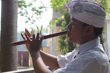 Portrait of Asian man wearing balinese traditional cloth playing bamboo flute in outdoor park