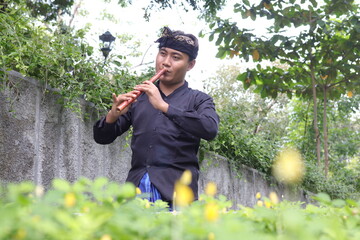 Portrait of Balinese man playing traditional bamboo flute at park in the morning