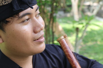 Portrait of Balinese man playing traditional bamboo flute at park in the morning