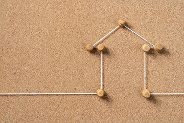 A minimalist representation of a house created with small wooden pushpins and white string on a...