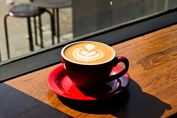 Close up view of hot cafe latte on the wooden table. red cup or mug. art. brown. dark, black, shadows. morning. relax, coffee time. cafe. coffee shop. sun shine, light.