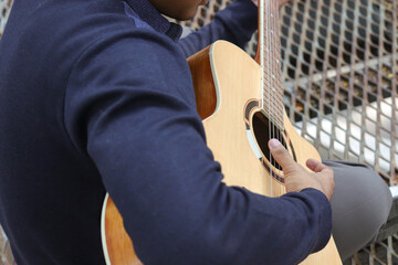 Portrait of Asian man playing guitar in a park during summer, surrounded by lush greenery and the peaceful atmosphere of the season