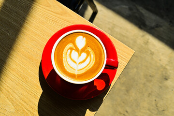 Top view of hot cafe latte on the corner wooden table. red cup or mug. art. brown. dark, black, shadows. morning. relax, coffee time. cafe. coffee shop. sun shine, light. high angle, above. close up.