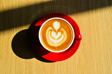 Top view of hot cafe latte on the wooden table. red cup or mug. art. brown. dark, black, shadows. morning. relax, coffee time. cafe. coffee shop. sun shine, light. high angle, above. close up. ceramic