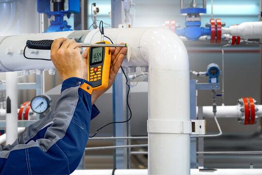 Worker measuring temperature on industrial pipeline with digital device, inspection and control of heating system, maintenance and engineering. Engineering.