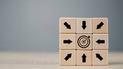 Wooden blocks with black arrows pointing toward a central target icon represent business focus, strategic direction, and goal achievement through teamwork, exploration, and problem-solving mindset.