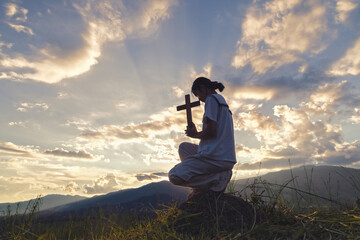 A girl holding a cross kneeling down praying to God