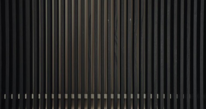 Aesthetic view of closely spaced vertical lines in varying shades of dark brown and black, creating a minimalist modern art effect. Closeup on wall with wooden panels in modern apartment