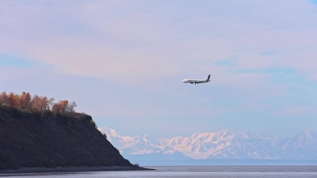 Scenic view of aircraft approaching Anchorage airport against snow-covered mountain range. Stunning Anchorage landscape with cargo plane preparing to land against Alaskan mountain scenery.