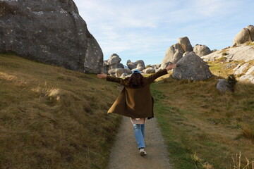 A person walks with outstretched arms down a path, surrounded by massive limestone boulders at Castle Hill (Kura Tawhiti), Canterbury, New Zealand, in May 2025. Capturing freedom in nature. © Chonlatit