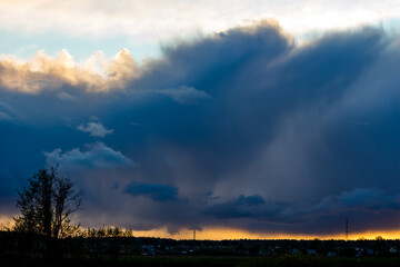 Dramatic dark storm clouds loom over a distant landscape, illuminated by a warm golden sunset glow at the horizon, creating a striking contrast