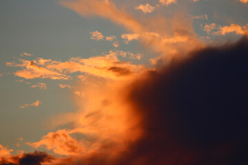 Vibrant orange and red clouds illuminated by golden hour light, contrasting with dark storm clouds...