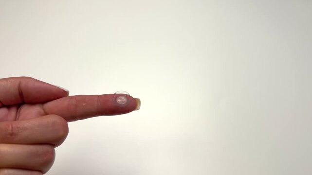 Close-up on a white background is a hand with a transparent contact lens on its finger. The concept of vision correction, ophthalmology, eye care and protection. High quality 4k footage