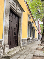 Yellow colonial facade with stone base and wooden door along sidewalk