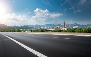 Fototapeta premium Open highway leading to a large industrial facility with mountains and clear sky, representing progress and energy