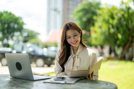 Asian woman working remotely outdoors using laptop - Powered by Adobe