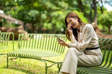 Woman smiling, laughing, holding smartphone outdoors in park