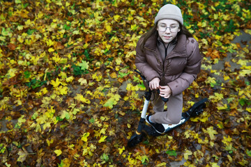 Young Woman Riding Electric Scooter through Autumn Leaves in Cozy Attire