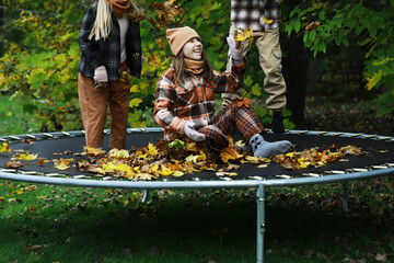 Autumn Fun: Kids Enjoying Leaves on Trampoline in Cozy Fall Clothing