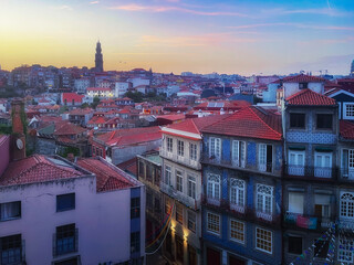 An evening panoramic view of the Porto skyline in Portugal with the Clerigos Tower in the background, traditional buildings with red roofs and tiled facades fill the foreground at sunset