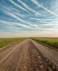 Long dirt road stretching through green fields under a vast sky