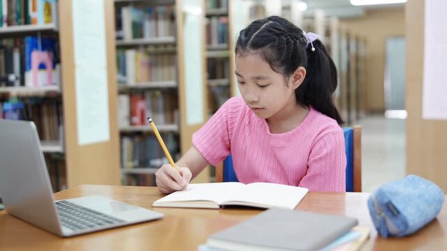 Focused girl doing homework and online learning at library using laptop. Concept of remote learning. Time management. Back to school. Education concept.