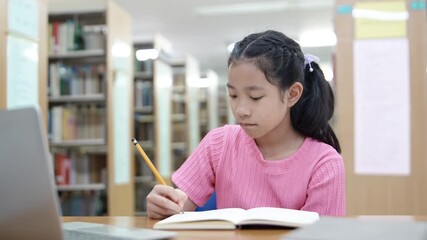 Focused girl doing homework and online learning at library using laptop. Concept of remote learning. Time management. Back to school. Education concept.