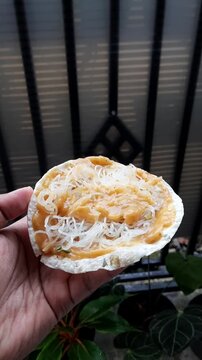 POV of a hand holding kerupuk kuah with noodle topping, traditional Indonesian street snack made from cassava crackers and spicy sauce